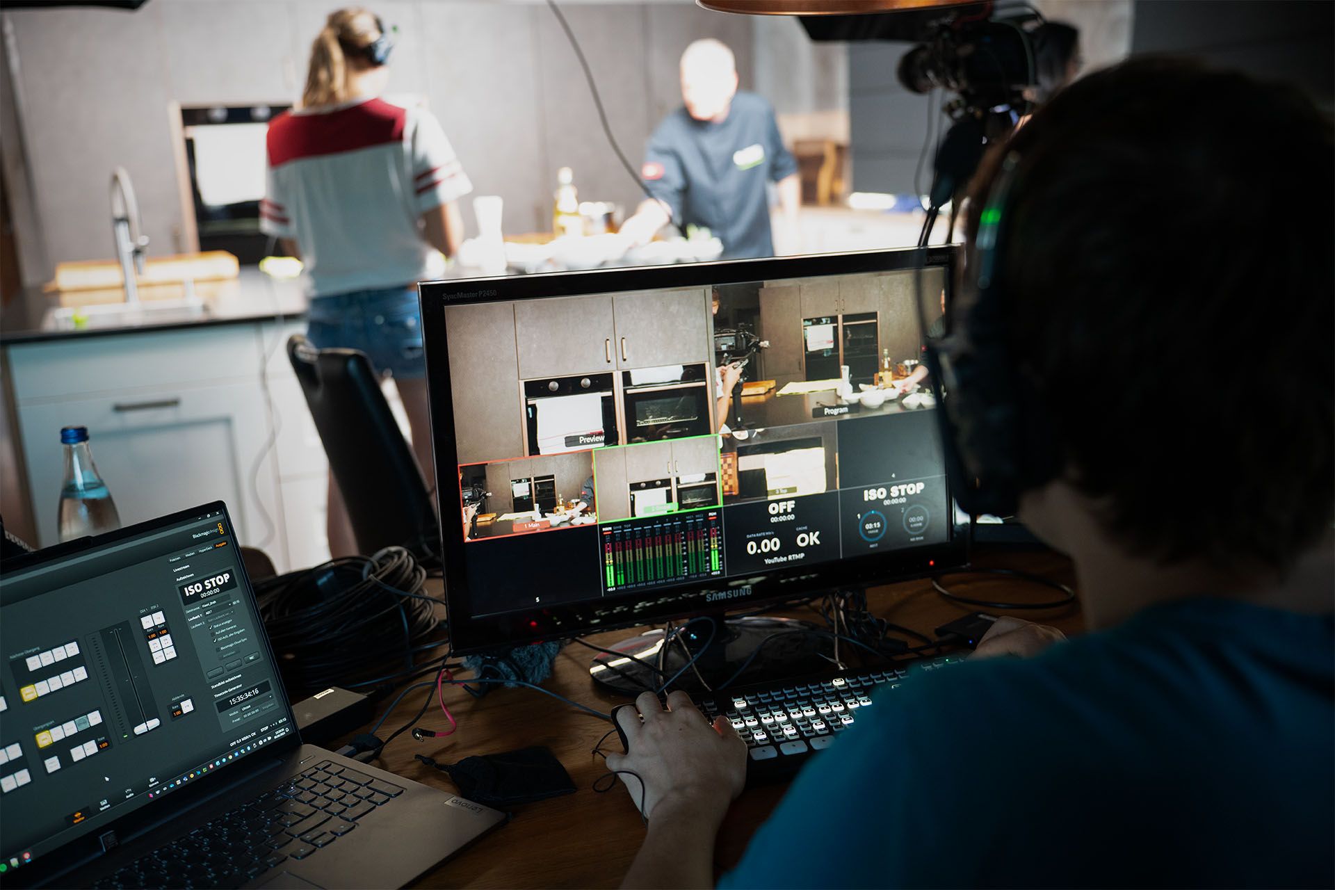 Monitor mit Live-Bild einer Küchenaufnahme während einer Videoproduktion, mit mehreren Kameraeinstellungen und einem Bedienpult im Vordergrund.